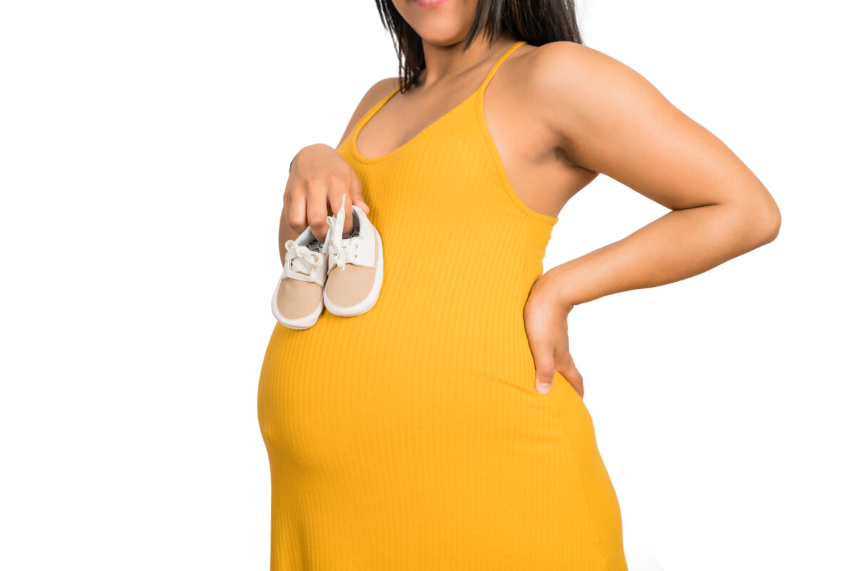 ANTENATAL DENTAL VISITS : An illustration of a happy pregnant woman holding shoes on belly